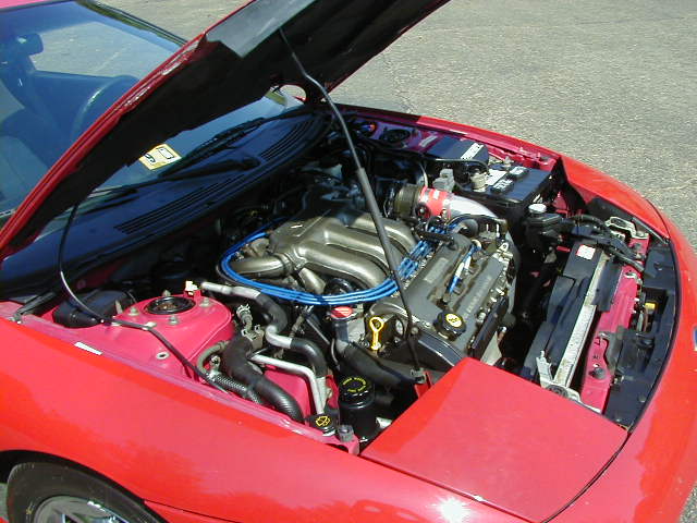 red car's engine bay with hood open, showing engine components and battery