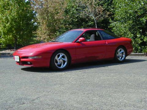1997 Ford Probe - A red 1997 Ford Probe GT is parked on asphalt, with trees in the background. The car features aftermarket wheels and a sunroof.
