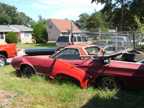 1966 Ford Ranchero - A red vehicle, possibly a Ranchero, sits in a yard with a separate fender and other parts.