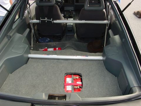 1986 Ford Mustang - The interior of a car is shown, with a focus on the trunk area containing a battery and safety equipment.