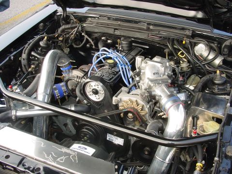 1986 Ford Mustang - Customized engine bay a turbocharger and polished intake piping, with a Ford logo on the radiator cover.