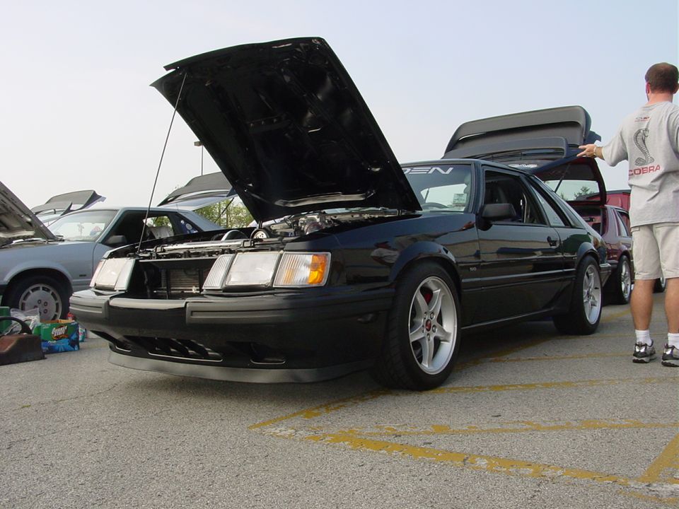 Black 1986 Ford Mustang coupe with hood and trunk open, parked next to another car