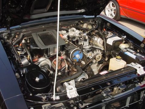 1986 Ford Mustang - The engine bay of a 1986 Ford Mustang, a turbocharger and custom blue pulley, with another vehicle visible in the background.