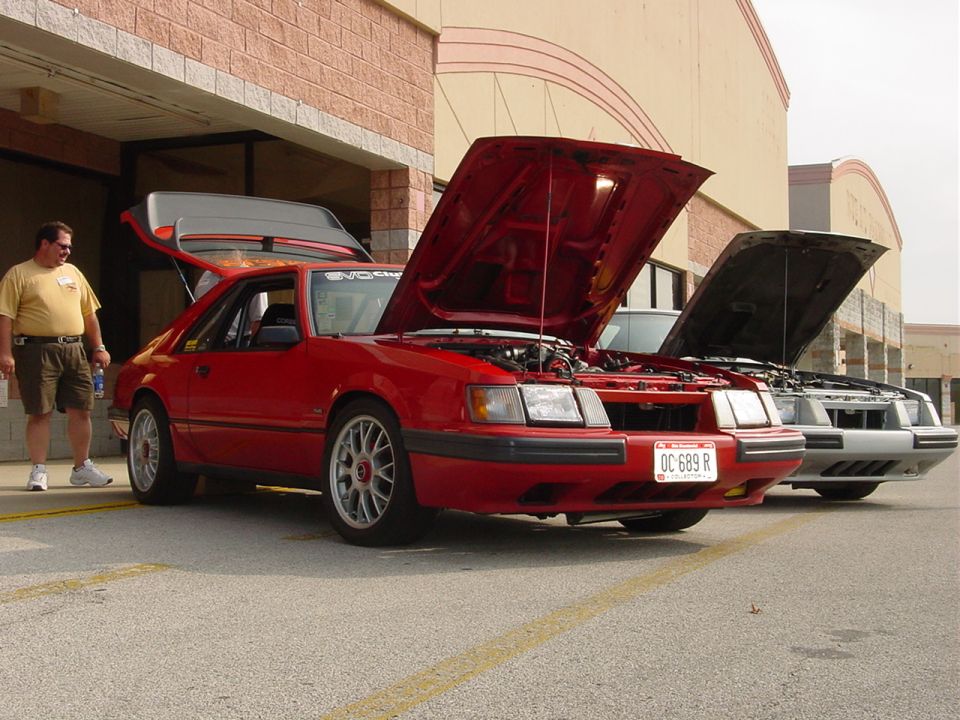 Red coupe with hood and trunk open, parked next to a silver coupe
