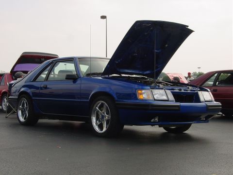1986 Ford Mustang - A blue 1987 Ford Mustang coupe is displayed with its hood open at an outdoor car event.