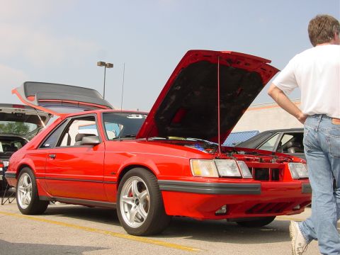 1986 Ford Mustang - A red coupe's hood and trunk are open, revealing the engine bay and cargo area at an outdoor event.