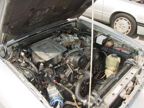 1986 Ford Mustang - The engine bay of a 1986 Ford Mustang is shown, with a portion of another silver vehicle visible in the background.