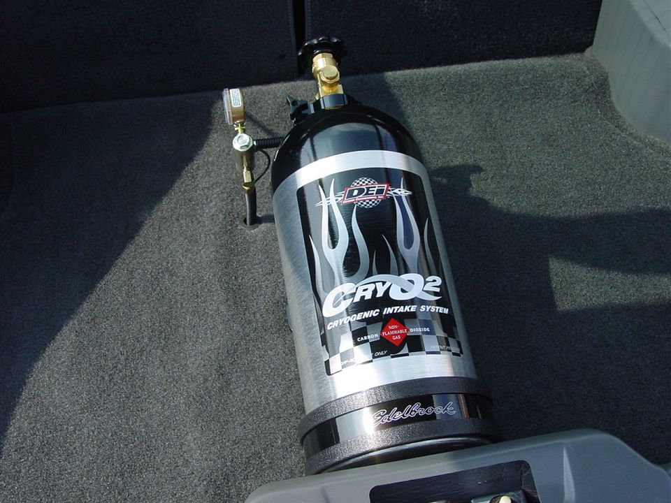 Nitrous oxide tank with Edelbrock base and "CRYQ2" graphics, mounted in a car's carpeted interior