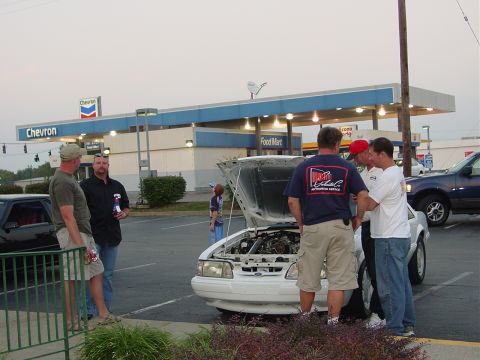 1986 Ford Mustang - A group of men gather around a white 1986 Ford Mustang with its hood open at a gas station.