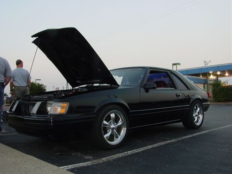 1986 Ford Mustang - Black 1986 Ford Mustang coupe with hood open, parked in a lot.
