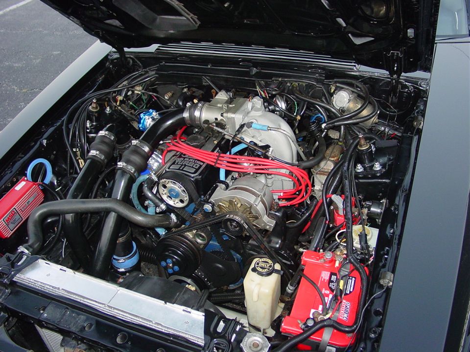 Engine bay with a turbocharger, red spark plug wires, and a red battery