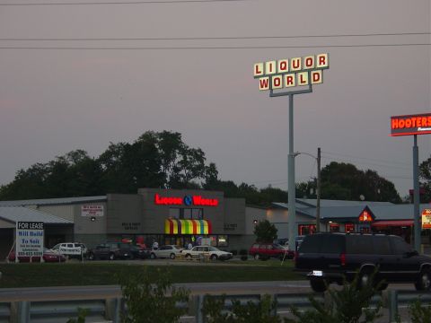 1986 Ford Mustang - A dark SUV is parked in front of a strip mall "Liquor World" and "Hooters" signage.