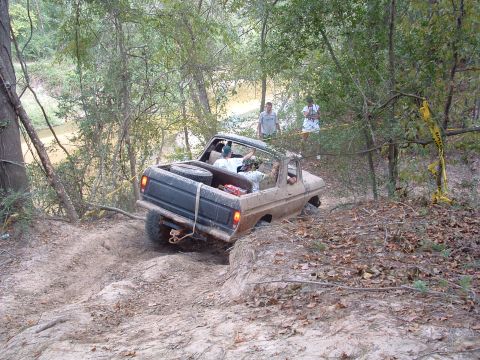 1993 Ford Bronco - This old Ford truck is navigating a challenging off-road trail near a wooded area and a creek.