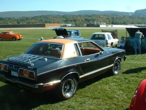 1978 Ford Mustang II - A black 1978 Ford Mustang II coupe with a tan roof sits on a grassy field next to other vehicles.