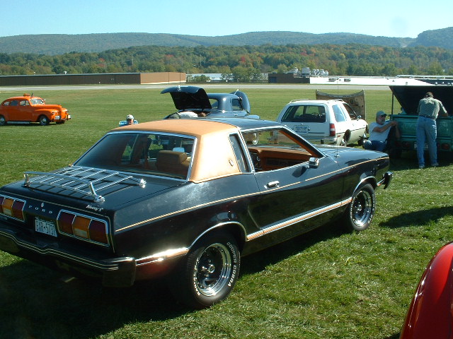 Black 1978 Ford Mustang II coupe with a tan vinyl roof and a rear luggage rack, viewed from the rear three-quarter angle