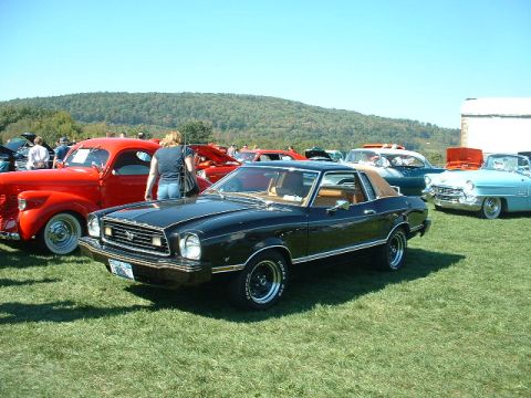 1978 Ford Mustang II - A black 1978 Ford Mustang II coupe, distinguished by its tan vinyl roof, is displayed at an outdoor car show alongside other classic vehicl…