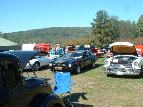 1978 Ford Mustang II - Multiple classic cars are parked on a grassy field under a clear blue sky.