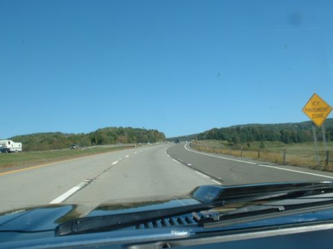 1978 Ford Mustang II - A view from inside a vehicle driving on a highway with trees and hills in the background.