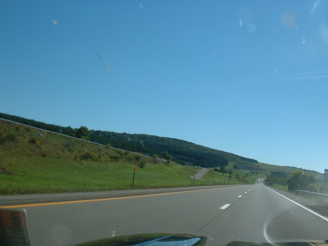 Highway scene with a blue sky and green hills, seen from a car's perspective
