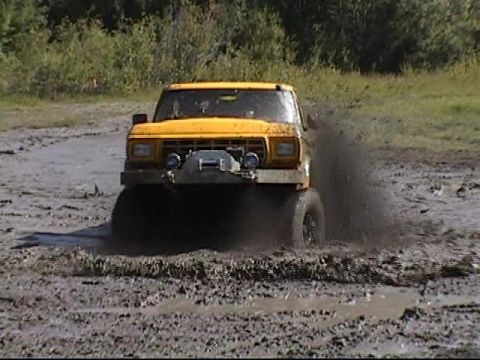 1979 Ford F-250 - Yellow 1979 Ford F-250 driving through mud, kicking up a large spray.