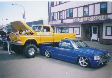 1979 Ford F-250 - A yellow 1979 Ford F-250 is parked next to a blue lowered Mazda B-series truck in front of the Mile Zero Hotel.