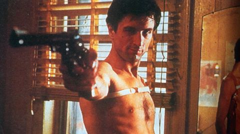 1995 Ford Bronco - A man aims a handgun directly at the viewer, with a white band across his chest.