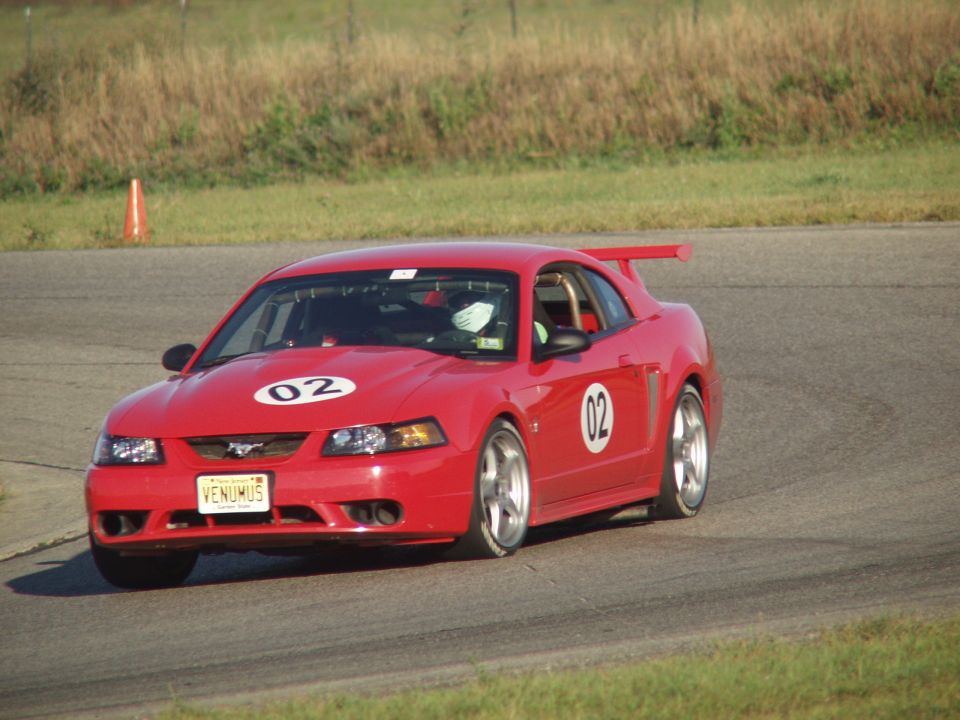 Red 2000 Ford Mustang with racing numbers '02' on hood and door, on a race track