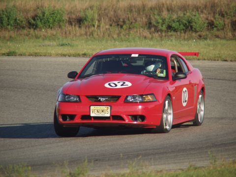 2000 Ford Mustang - A red 2000 Ford Mustang with racing numbers navigates a track on a sunny day.