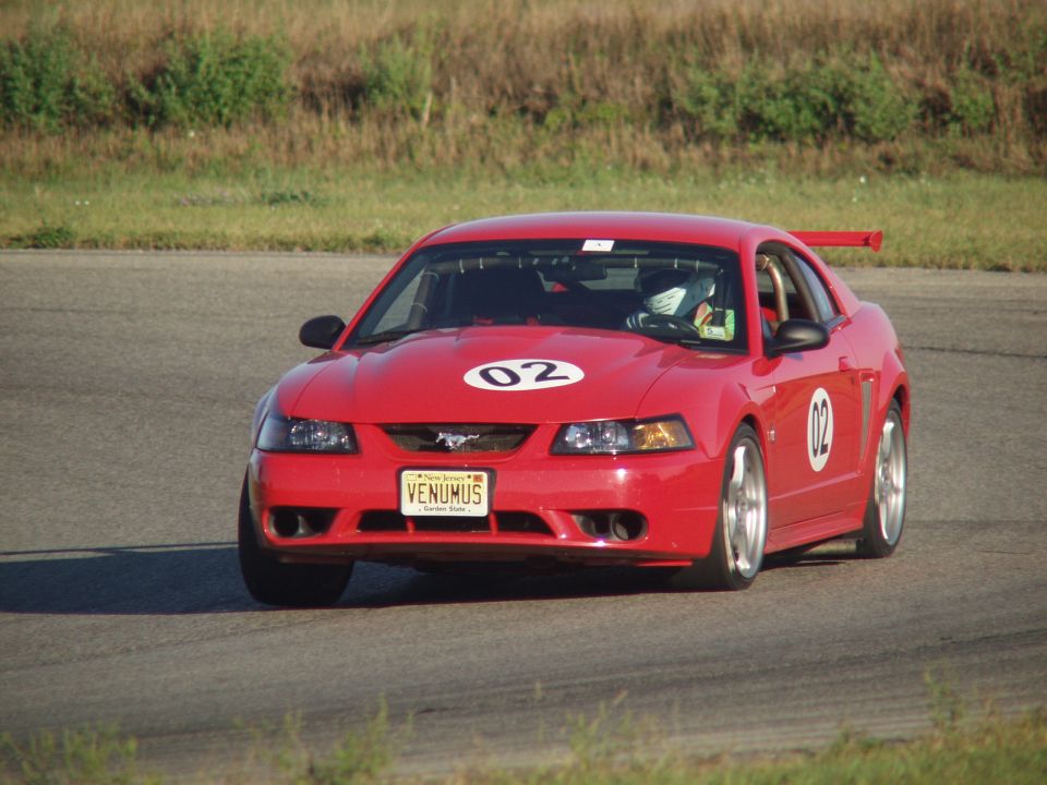 Red 2000 Ford Mustang with racing numbers 02 on hood and door, on a race track
