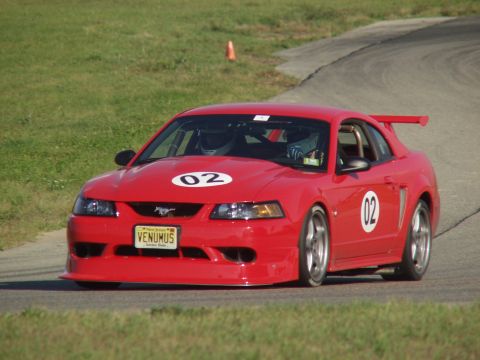 2000 Ford Mustang - A red 2000 Ford Mustang race car with racing decals navigates a turn on a sunny day.