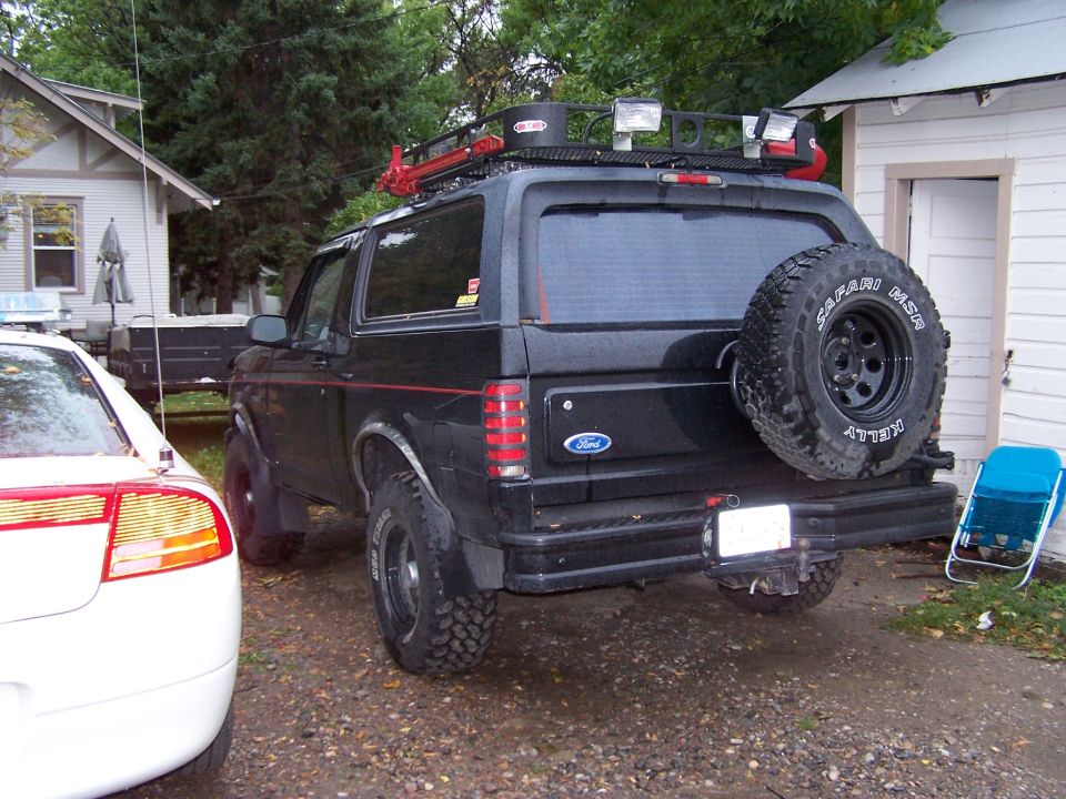Black 1996 Ford Bronco parked in a driveway, spare tire on back, roof rack with lights