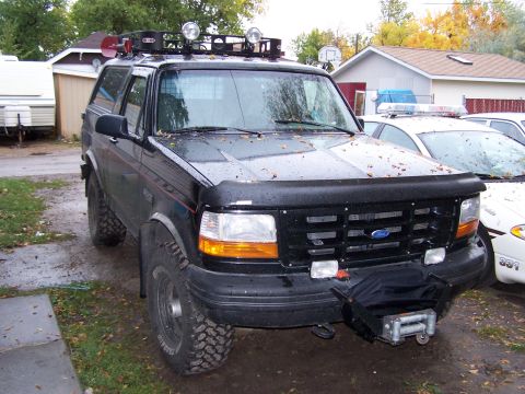 1996 Ford Bronco - A black 1996 Ford Bronco is parked in front of a house, with a police car visible in the background.