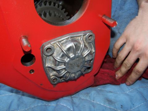 1979 Ford F-150 - A person's hand is visible, wiping a red cloth near a red transmission housing with a metal plate and visible gears.