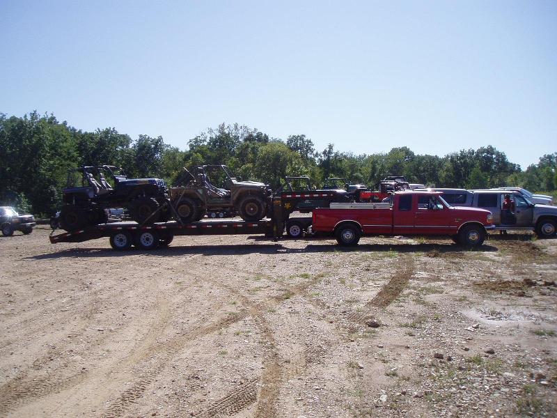 Red pickup truck towing trailer with ATVs and a Jeep-like vehicle
