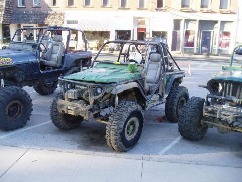 1992 Ford Bronco - Several custom off-road vehicles are parked in a lot, modified for terrain.