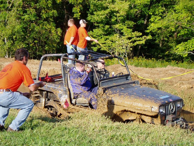 Jeep stuck in mud pit with people trying to pull it out