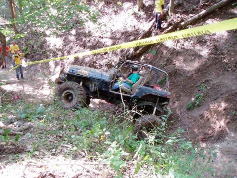 1992 Ford Bronco - An off-road vehicle navigates a steep, wooded trail with caution tape marking the path.