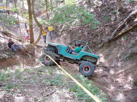 1992 Ford Bronco - An off-road vehicle navigates a challenging incline in a wooded area, with onlookers observing the difficult climb.