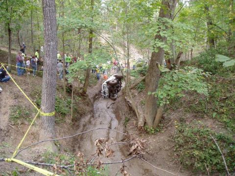 1992 Ford Bronco - An off-road vehicle has gotten stuck and flipped on its side in a muddy, wooded area.