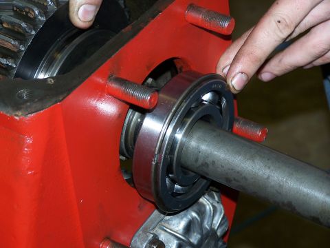1979 Ford F-150 - Mechanic's hands guide a bearing into a red housing with a metal shaft.