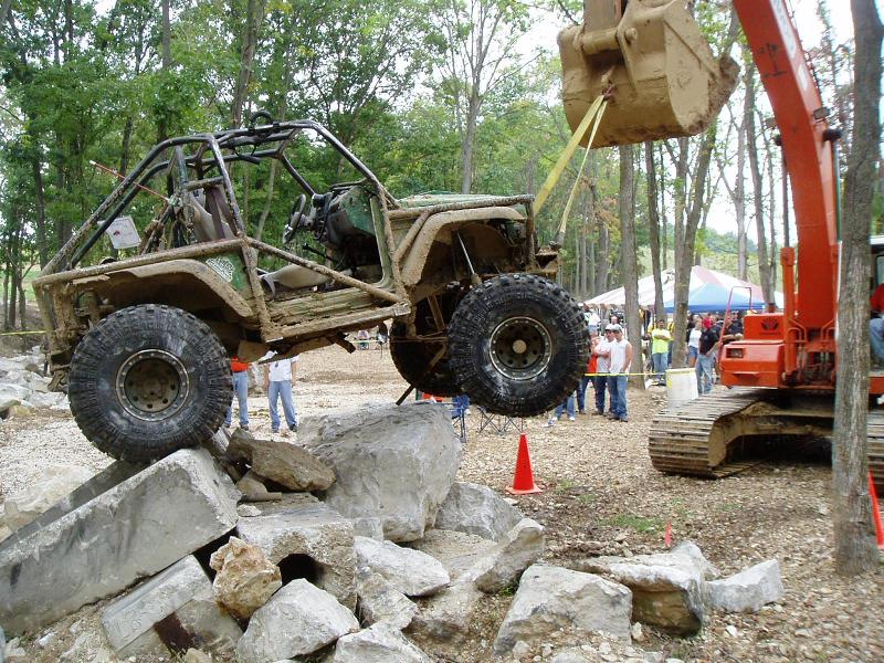 off-road buggy lifted by excavator over rocks