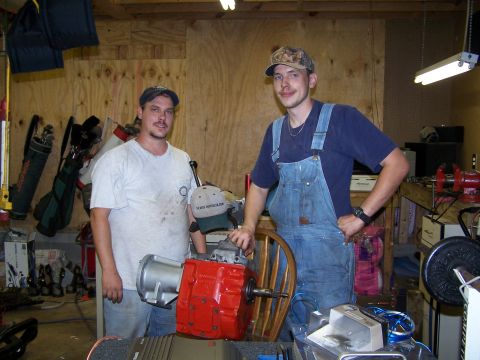 1979 Ford F-150 - Two men stand in a cluttered garage next to a red transmission assembly.