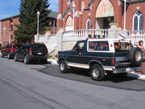 1992 Ford Bronco - A line of wedding vehicles, including a decorated Ford Bronco, parked outside a church.