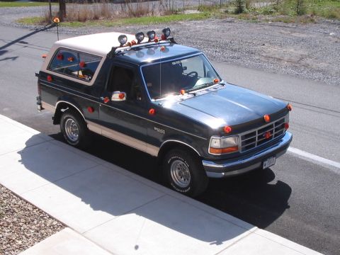 1992 Ford Bronco - This Ford Bronco is parked on a residential street with a sidewalk and gravel lot in the background.