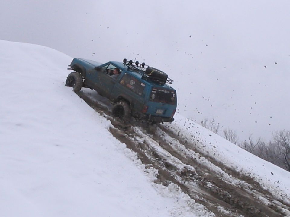 Blue SUV with roof rack and spare tire driving up a snowy, muddy incline