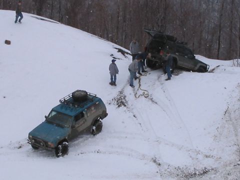 1992 Ford Bronco - People attempt to recover a stuck off-road vehicle in a snowy, wooded area.