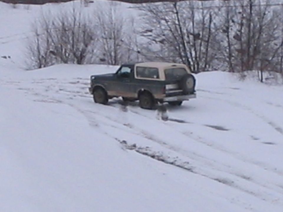 Dark blue 1992 Ford Bronco with a tan top driving in snow, spare tire mounted on rear