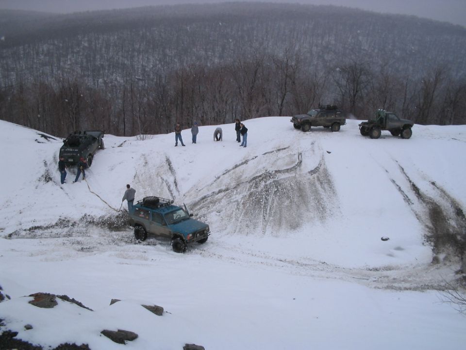 Off-road vehicles navigating a snowy hill with people assisting