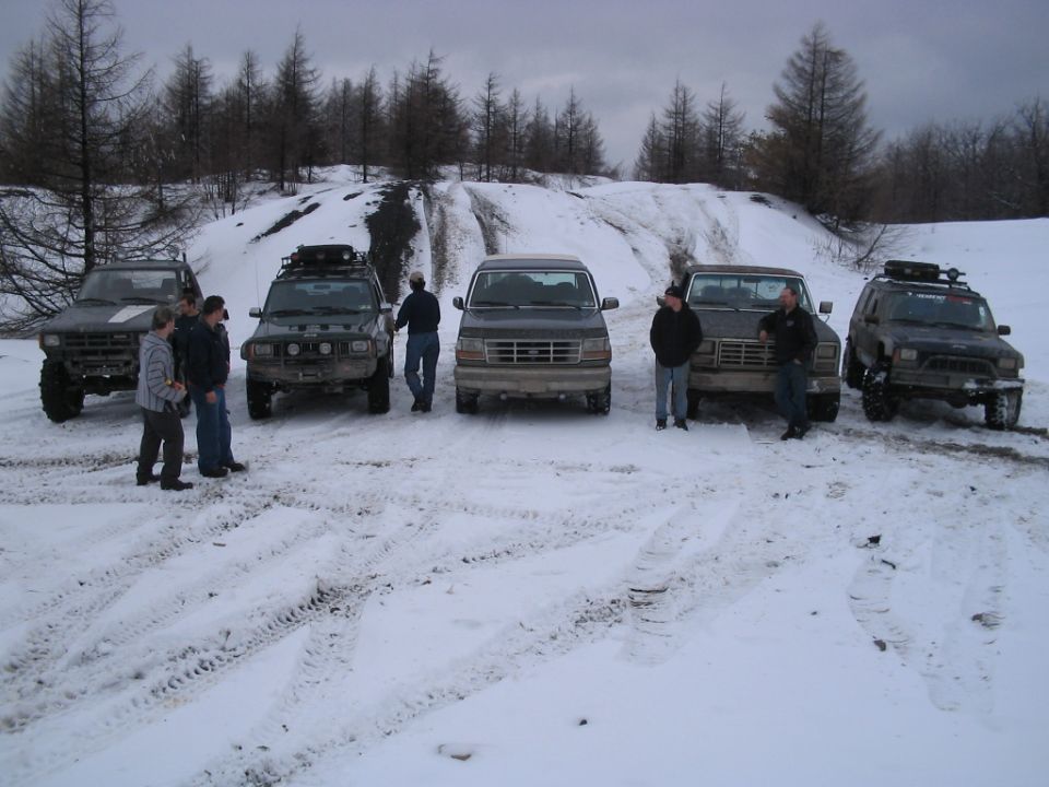 Five SUVs and trucks parked in snow, with people standing around them