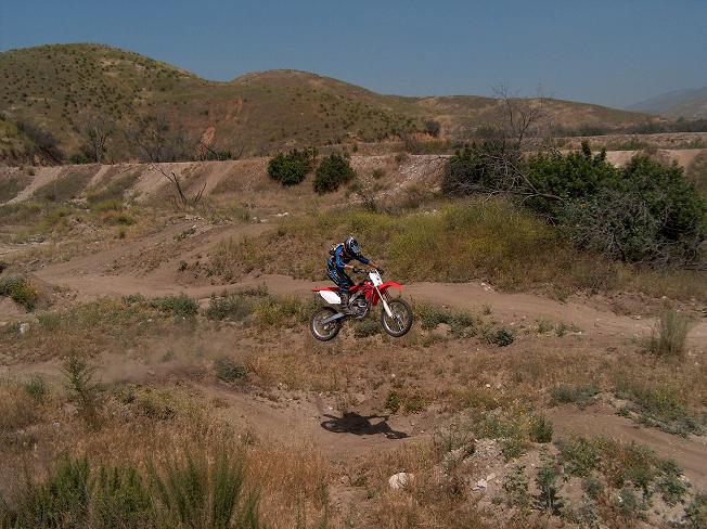 Rider jumping a red and white dirt bike on a dusty trail through dry scrubby hills